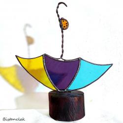 Cet objet vitrail décoratif est une coccinelle orange qui monte le long du manche d'un parapluie multicolore