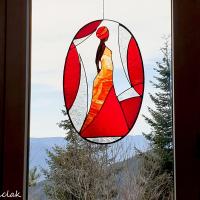 Présentation du vitrail décoratif femme en robe rouge suspendu devant une fenêtre.